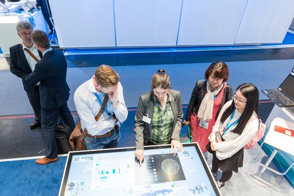 Am Touchtable wird mehreren Messebesuchern die Projektidee interaktiv erklärt.