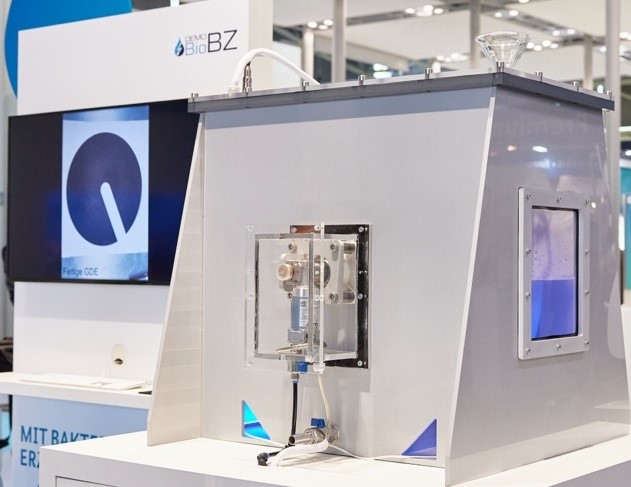 Auf der IFAT 2022 gezeigte Miniatur-Biobrennstoffzelle in Plexiglas-Box und seitlichem Sichtfenster mit drehenden Elektroden und einer Stromableitung über die Welle mittels Schleifkontakten.