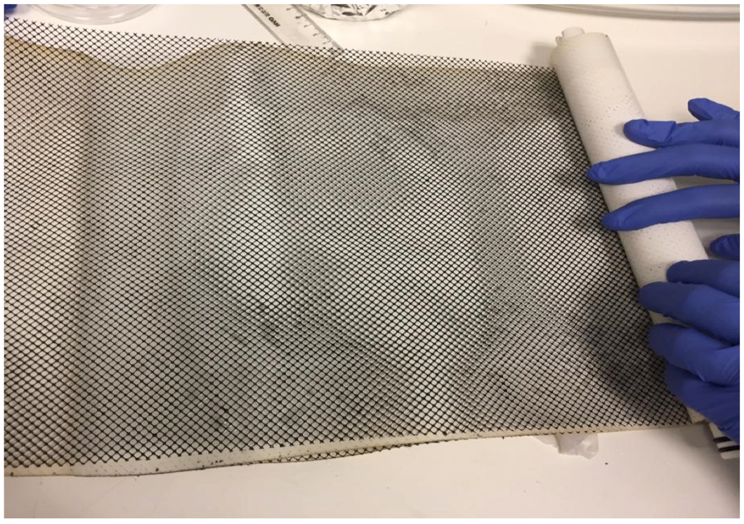 Seen in the figure is a black colored polymer mesh that is being rolled into a spiral wound membrane module for traetment of brackish water. The module is approx. 30 cm long. This black coating consists of an electrically conductive carbon material named laser-induced graphene.